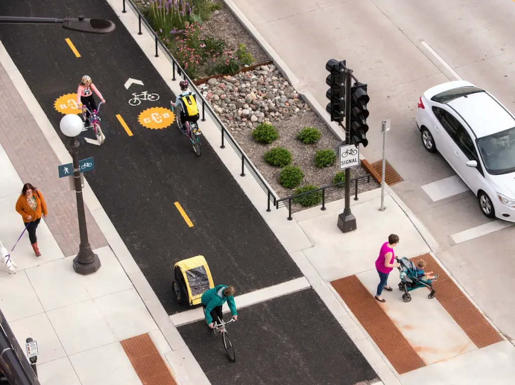 A bird's-eye view of a street in downtown Saint Paul, with people of all ages walking and cycling on a sidewalk and protected bike lane.